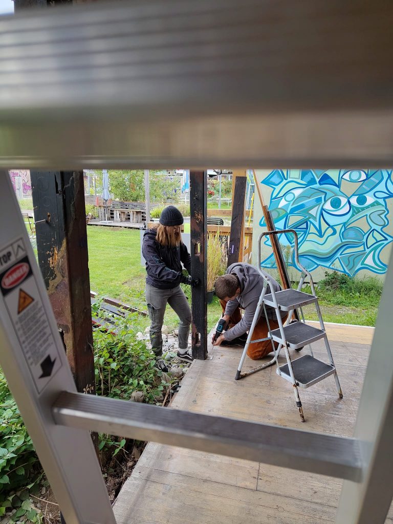 Helfer*innen Anner und Fabienne fixieren einen Holzbalken