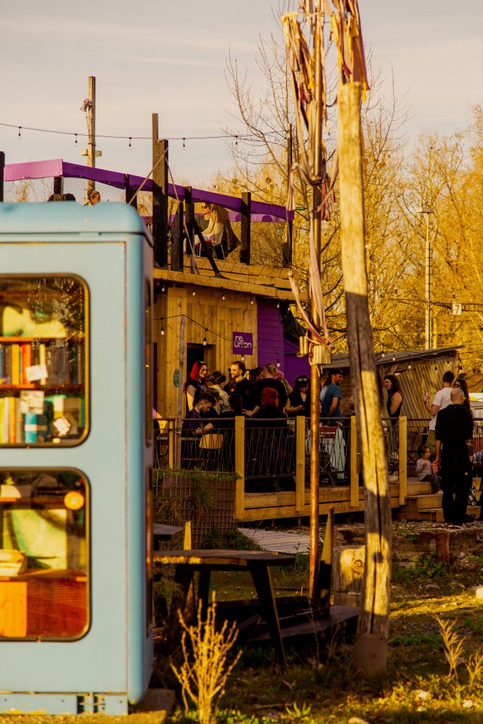 Außenansicht reUnion mit Gästen, im Vordergrund unscharf die Telefonzelle mit Büchern auf dem Weg in den Holzpark